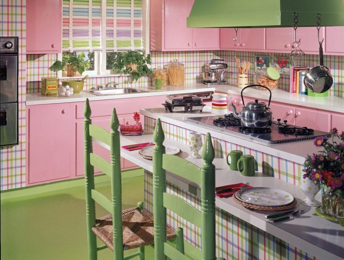 cuisine de couleur rose avec des meubles hauts et bas rose sol et chaises verts et ilot central à rayures
