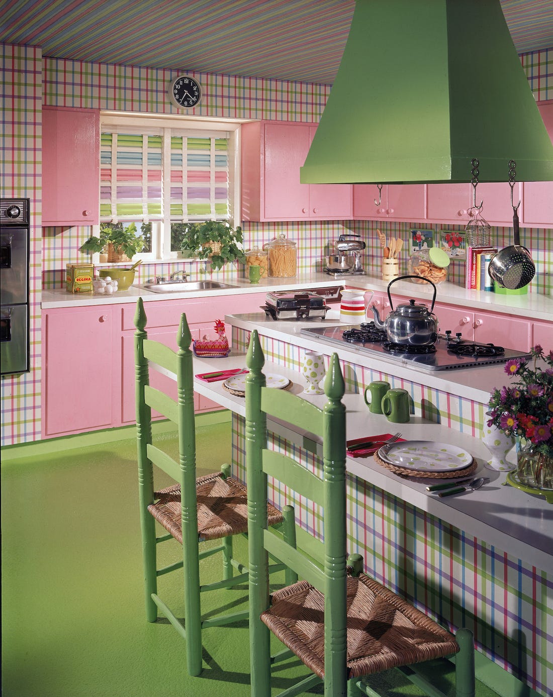 cuisine de couleur rose avec des meubles hauts et bas rose sol et chaises verts et ilot central à rayures