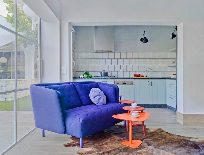 cuisne ouverte avec carrelage metro blanc sur salon avec tables basses oranges et canapé violet tapis fausse fourrure