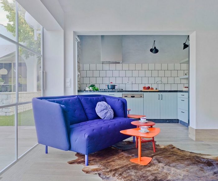 cuisne ouverte avec carrelage metro blanc sur salon avec tables basses oranges et canapé violet tapis fausse fourrure