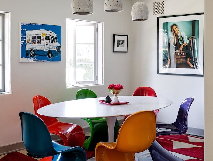 deco chaises dépareillées colroées autour d une table ovale de couleur blanche dans salon blanc avec tapis rouge et gris et art inspiration theme annee 70