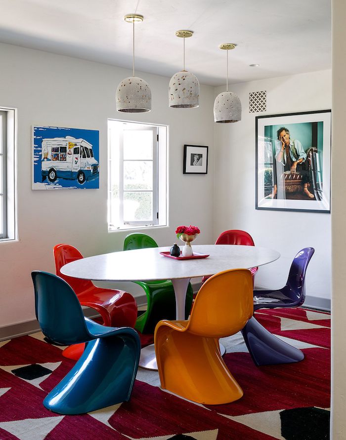 deco chaises dépareillées colroées autour d une table ovale de couleur blanche dans salon blanc avec tapis rouge et gris et art inspiration theme annee 70