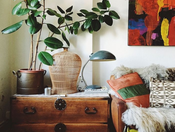 deco style année 70 avec commode de bois aux accents metalliques vase en rotin plante verte en pot canapé cuir marron et déco de coussins boheme chic