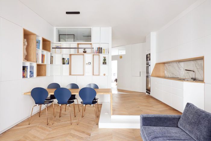 décoration appartement moderne avec parquet bois clair table bois et chaises bleues canapé gris credence marbre cuisine blanche et étagères blanches ouvertes dans meuble