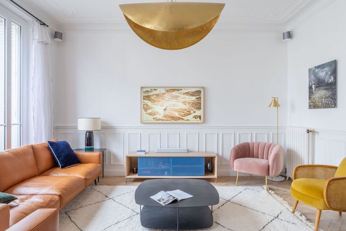 décoration salon appartement avec tapis blacn canapé de cuir marron faureuil jaune moutarde et rose poudré et table basse grise mur soubassement moulures