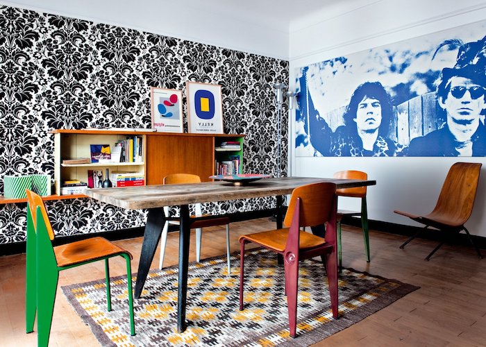 exemple de salle à manger style année 70 avec tapis coloré table bois et metal et chaises bois et metal mur papier peint noir et blanc fleuri deco ancienne