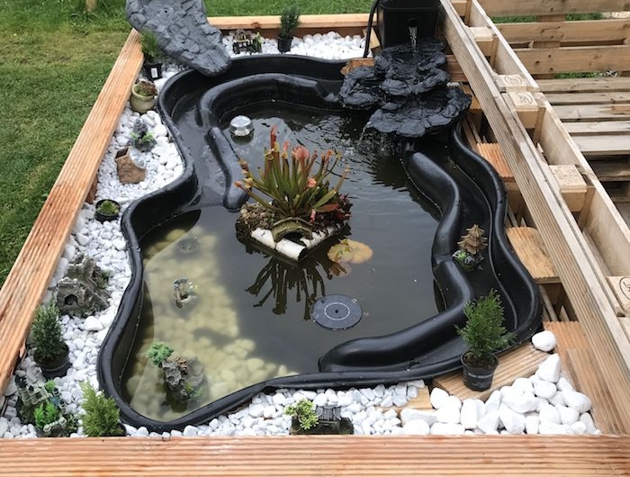 idee de bac de jardin en bois surélevé avec bassin préformé noir entouré de galets et petites plantes vertes et petit robinet