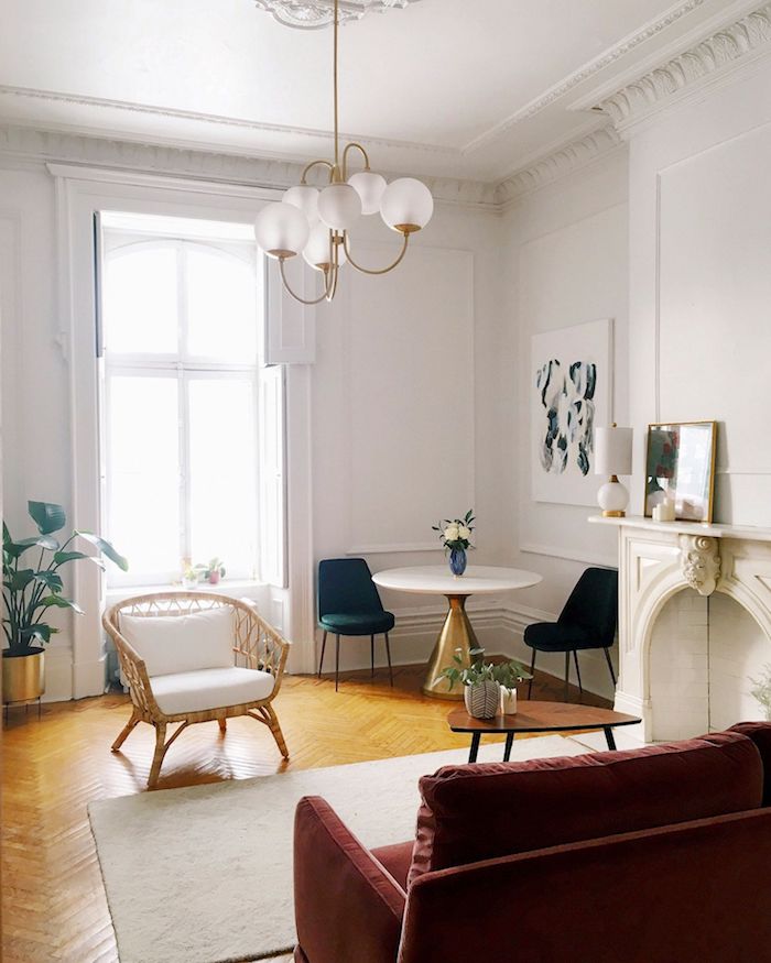 idée classique d appartement parisien avec parquet chevron chaise tressée canapé rouge tapis blanc coin table laiton et chaises vertes