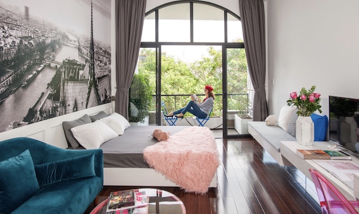 idée déco studio 20m2 avec lit gris et blanc plaid rose canapé bleu paon banc suspendu petit balcon pappier peint paysage photomural vue de paris