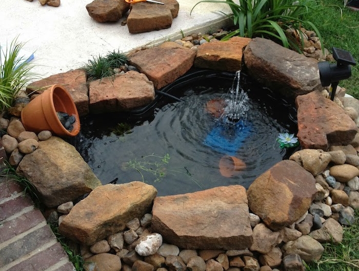 mini bassin de jardin entouré de galets et pierres plus grandes avec des pots de fleurs et de l eau dans un jardin