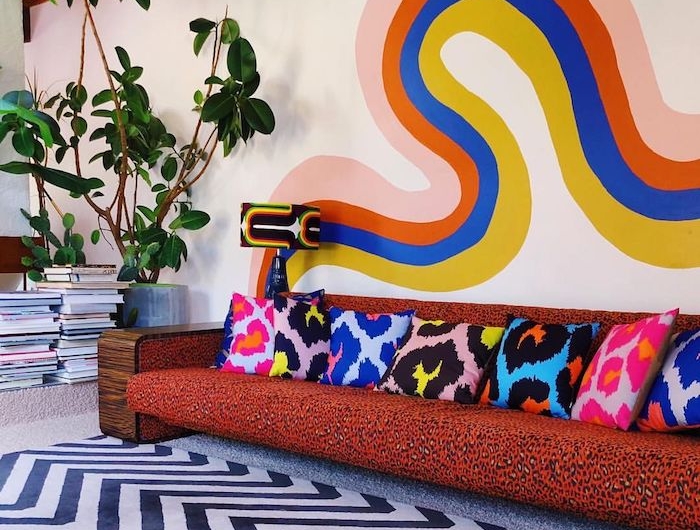 motif coloré mural deco psuchadélique deco salon vintage seventies avec canapé motif leopard coussins colorés plantes vertes et piles de magazines