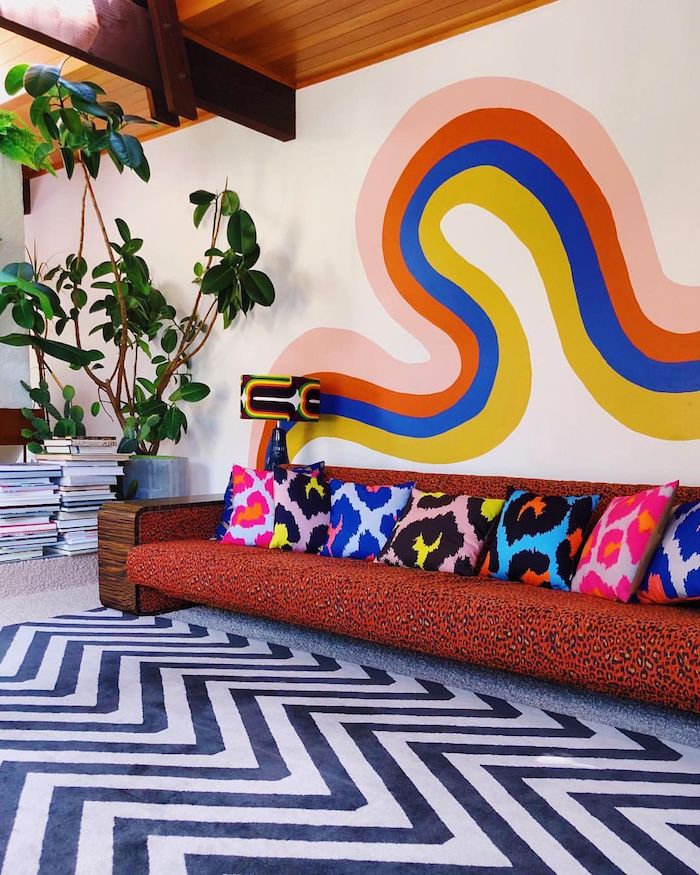 motif coloré mural deco psuchadélique deco salon vintage seventies avec canapé motif leopard coussins colorés plantes vertes et piles de magazines