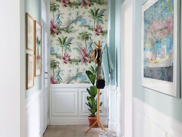 pan de mur décoré de papier peint tropical dans un couloir en blanc et bleu clair avec cadres decoratifs soubassement blanc idée déco couloiur lumineux