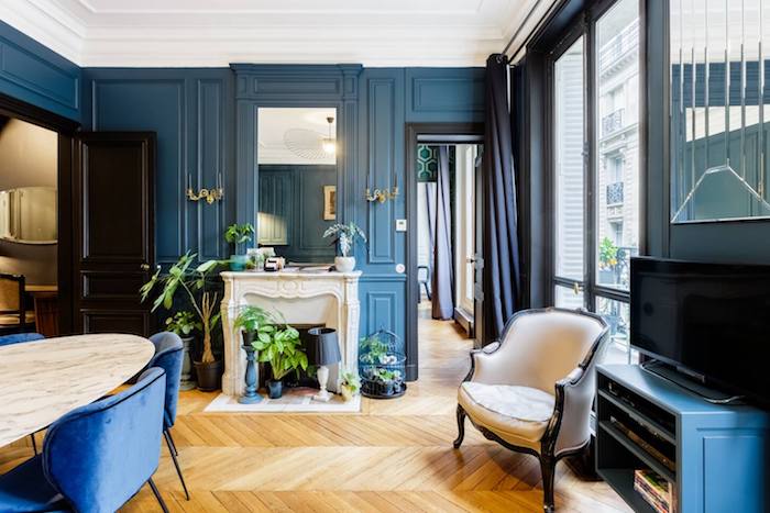 peinture murale bleu foncé parquet bois clair chevron cheminée blanche table marbre et chaises bleu marine décoration appartement moderne de luxe