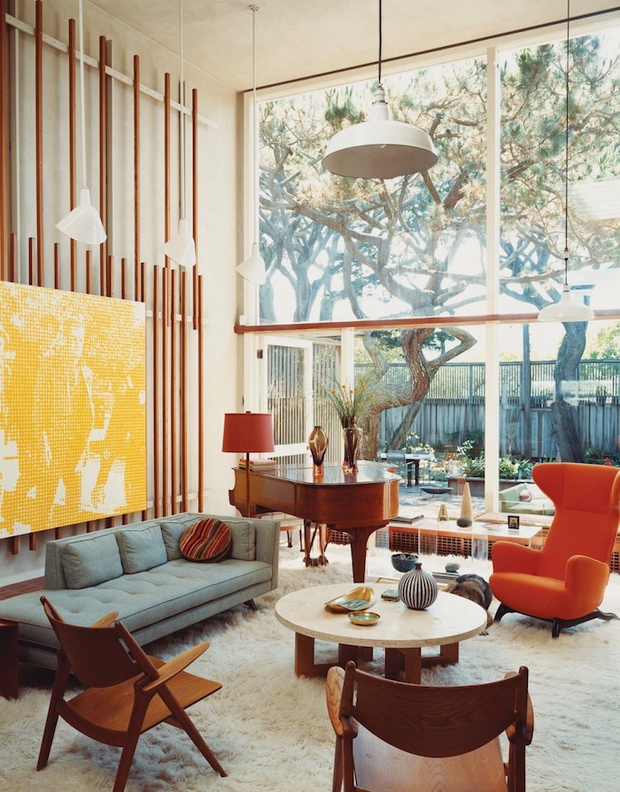 piano vintage de bois fauteuil oeuf orange canapé gris clair tapis blanc moelleux chaises bois et table basse bois et marbre tableau jaune enorme, déco années 70