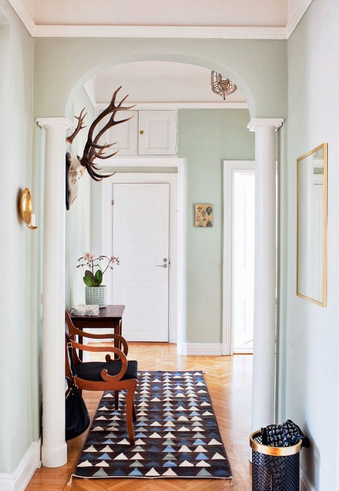 quelle couleur pour un couloir d entrée murs vert pastel colonnes blanches parquet clair tapis geometrique chaise bois et noir deco murale originale