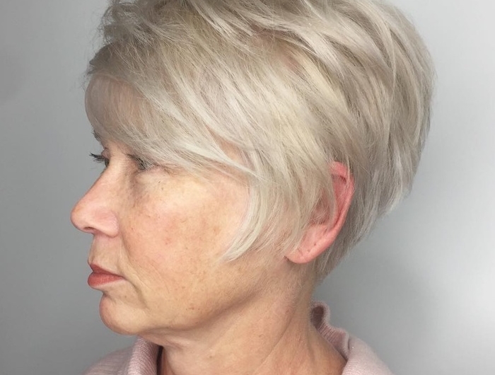 38 coiffure femme 60 ans épanouie femme avec un pull rose et cheveux blondes platinees