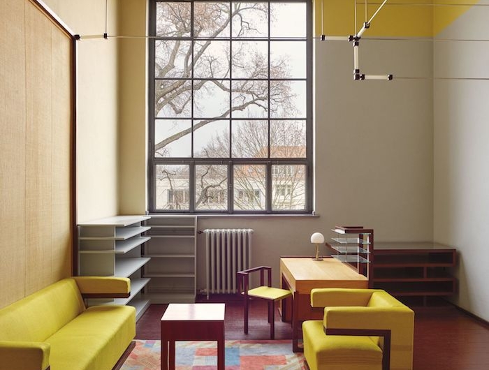 amenagement de bureau en style bauhaus des canapes jaunes et un tapis multicolore entoures des etageres originales