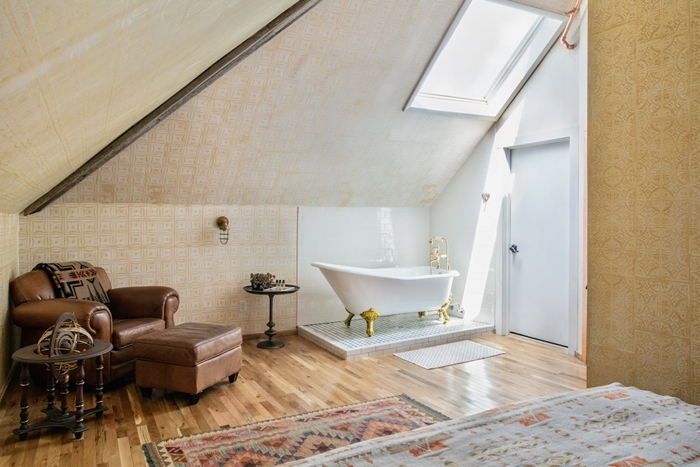 fauteuil cuir marron tapis motifs ethniques chambre avec salle de bain ouverte baignoire autoportante pieds dorés
