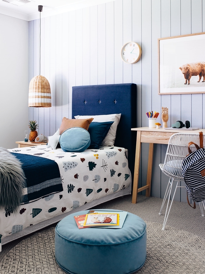 lit avec tete de lit dans une chambre enfant bureau bois clair revêtement mur panneaux bois horloge bois table de chevet bois ottoman bleu pastel