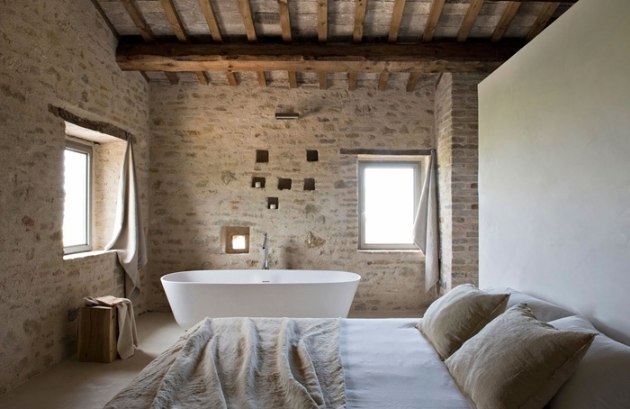 mur briques plafond avec poutres apparentes salle de bain dans chambre baignoire autoportante couverture de lit beige