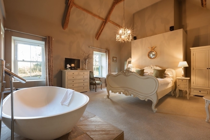 poutres bois apparentes baignoire dans chambre autoportante revêtement sol bois commode blanche miroir cadre or lampe de chevet