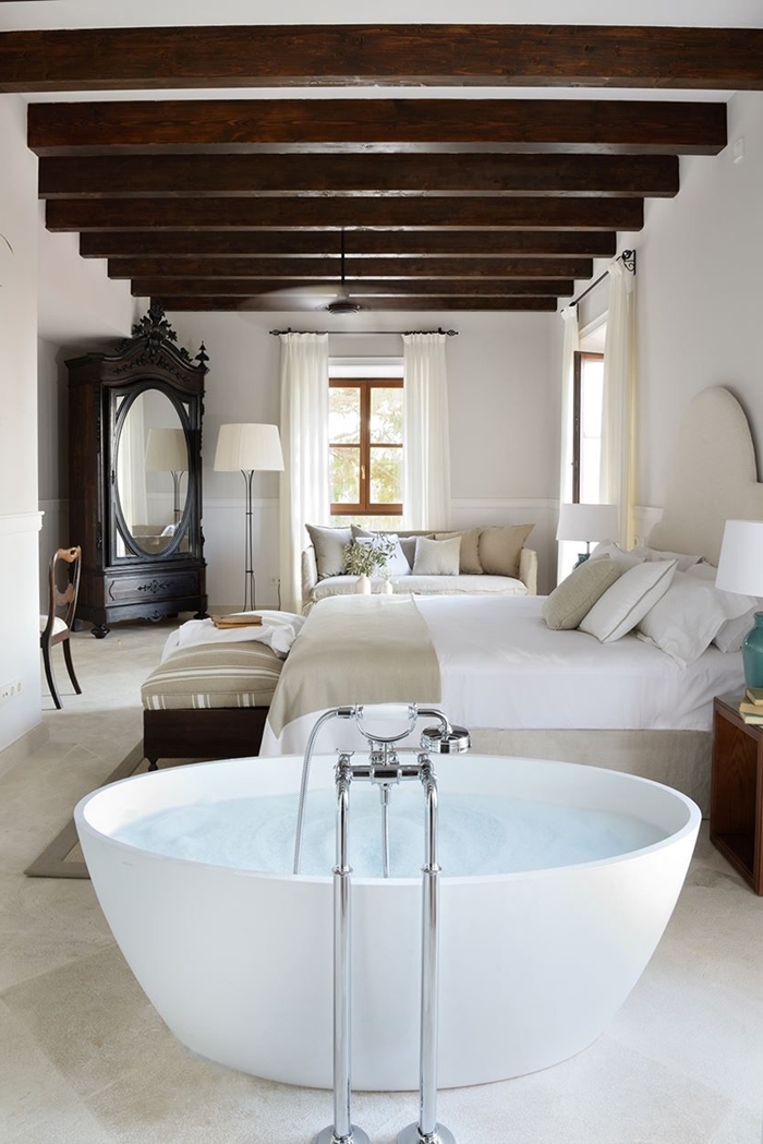 salle d eau dans chambre baignoire autoportante plafond blanc poutres bois foncé apparentes meuble bois foncé miroir ovale