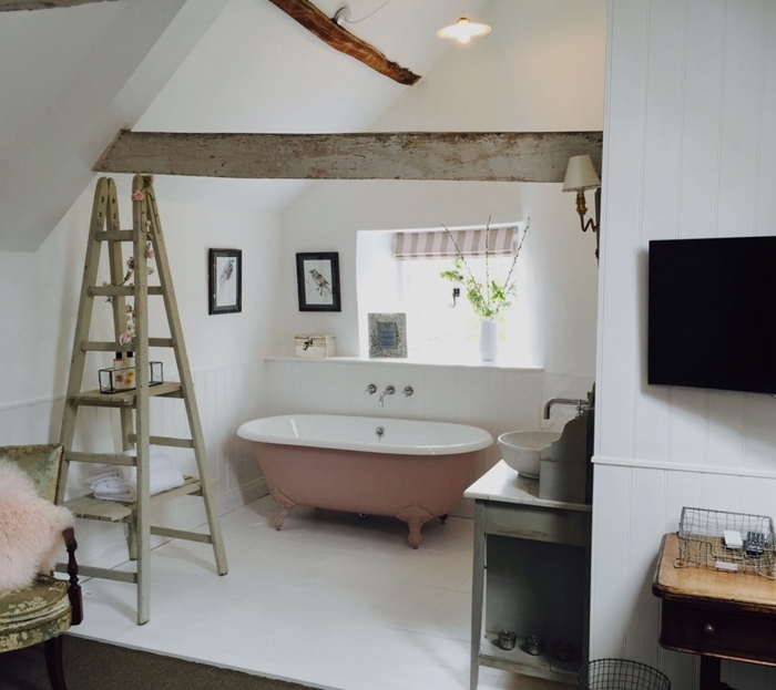 échelle décorative bois décoration sous combles chambre avec salle de bain baignoire rose et blanc chaise coussin fausse fourrure rose pastel