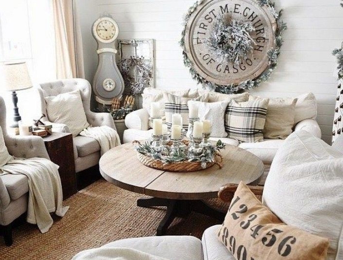 canapé et fauteuils gris et blanc tapis brut murs lambris blanc table bois brut centre de table bougies et branches de pin deco murale rondin