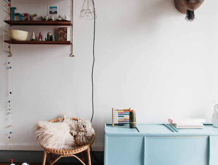 chaise en rotin meuble bas bleu nuit parquet couvert tapis fausse fourrure étagère bois brut murs blancs