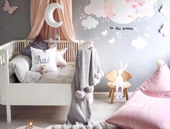 chambre bébé fille déco avec lit blanc à barreaux tapis doux blanc coussin d assise rose mur gris clar sur parquet bois clair coussins décoratifs