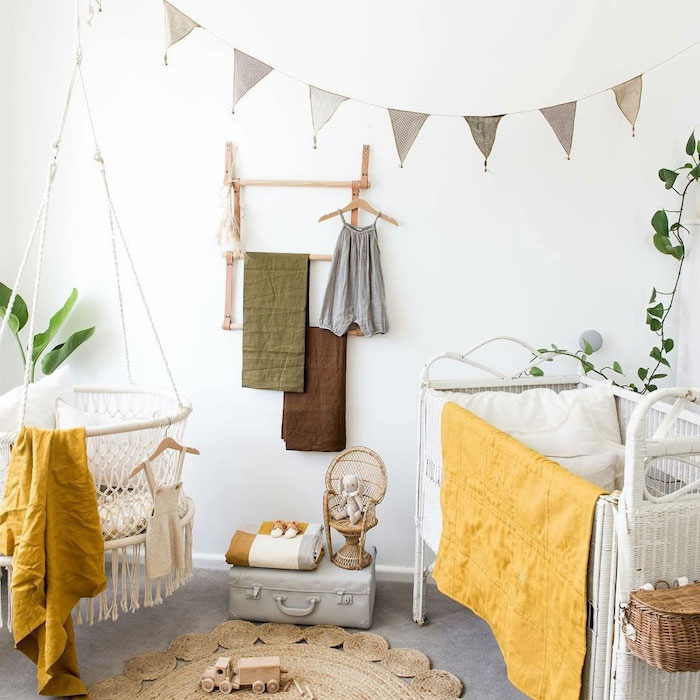 chambre bébé mixte décoré aux accents jaunes fauteuil suspendu blanc lit blanc metallique tapis rond vetements enfant suspendus sur des patères