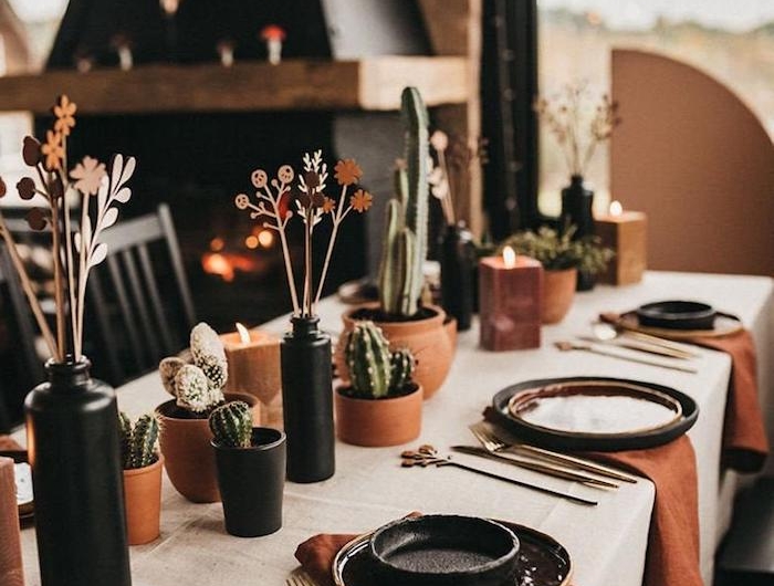 decoration de table originale avec des couverts et vases noirs des pots de cactus et nappes oranges une cheminee au fond de la piece