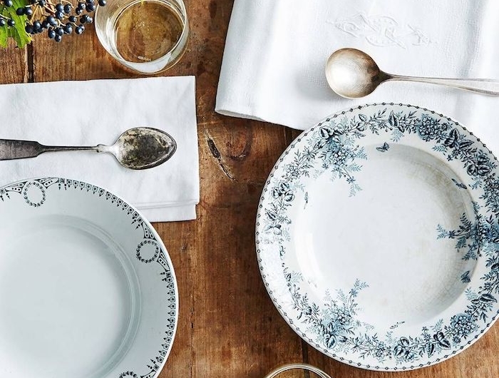 des assiettes de porcelaine bleu et blanc avec des ornament sur une table en bois des nappes avec des monogrammes et une branche de sureau comme decoration