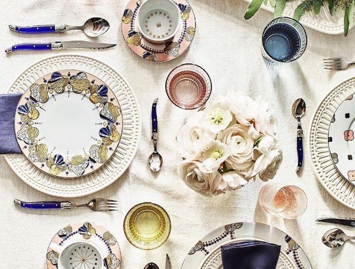 dresser une table a la francaise avec des assiettes multicolores en porcelaine bouquet de roses au centre de la table un cake saupodre dans un plateau garni des branches vertes