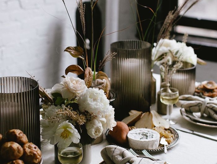 dresser une table en style automnale avec des fleurs blancs et des pommes grilles dqns des assiettes des ridaux noir et murs blanc