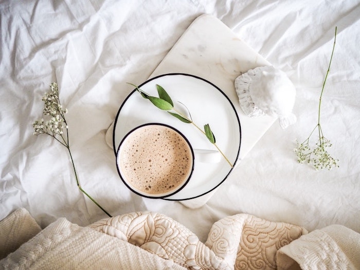 fond d ecran neutre et minimalistic avec une tasse de cafe au lit avec branches de plantes et des couettes