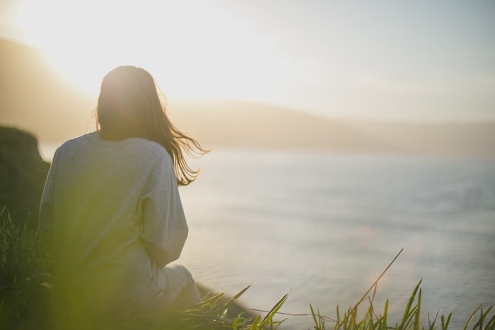 fond ecran aesthetic une fille assise sur l herbe regarde le soleil se couche au bord de la mer