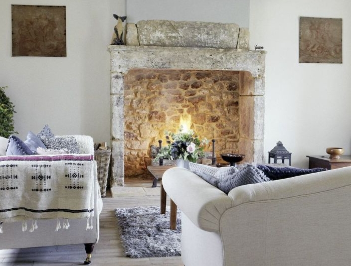 lustre elegant à mapilles canapés blancs décorés de coussins cocooning tapis moelleux cheminée de pierre table basse bois avec deco nature