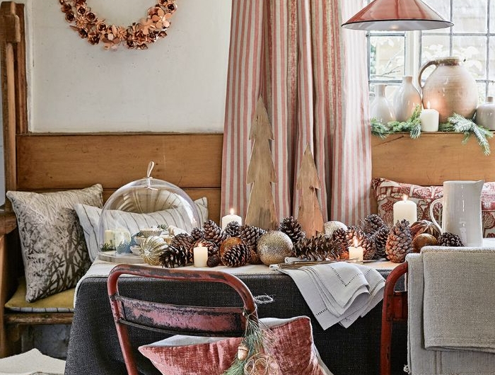 salle a manger rustique avec table décorée de nappe grise centre de table en pommes de pin et bougies chaie metal et banc de bois deco coussins