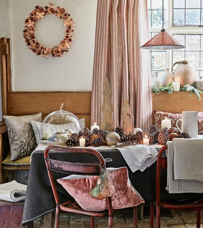 salle a manger rustique avec table décorée de nappe grise centre de table en pommes de pin et bougies chaie metal et banc de bois deco coussins