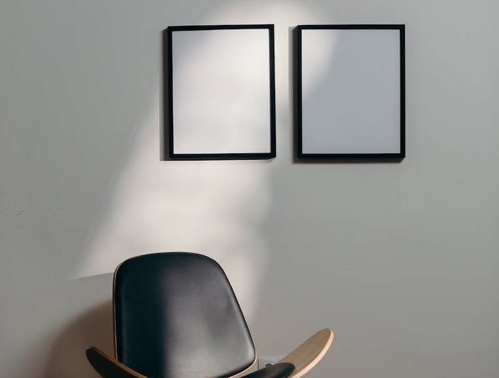 stylistique neutre et minimaliste teux tableaux blanches au mur sol en parquet et un fauteil en cuir noir