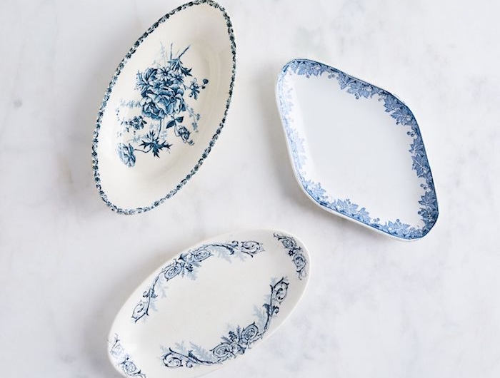 trois assiettes de porcelaine ornamentaux en bleu et blanc poses sur une surface de marbre blanc
