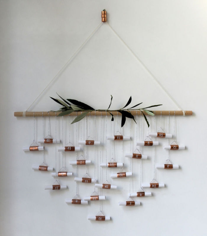 calendrier de l avent maison avec des petites lettres suspendues a une branche sur un mur blanc