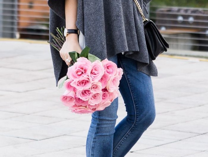 cape fourrure en gris combine avec des jeans et bottes noires une femme qui tient bouquet de roses