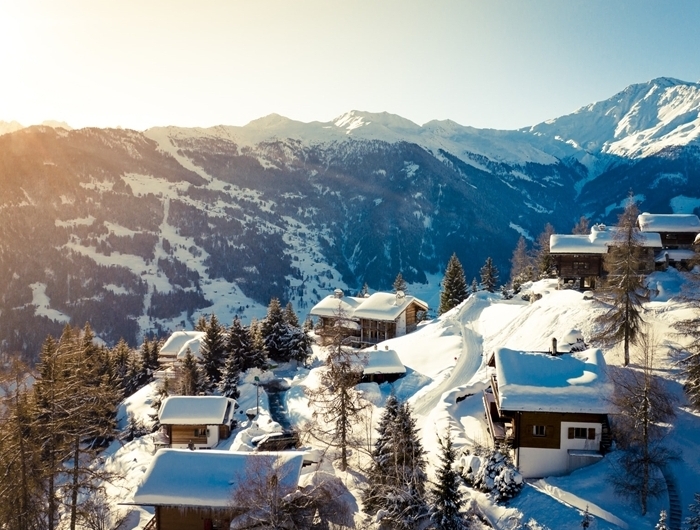 paysage montagne hiver rayons soleil sommets montagne enneigée village maison bois toit neige