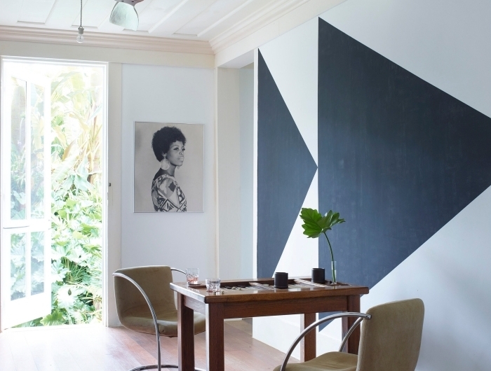 peinture murale géométrique triangles gris anthracite sur fond blanc table bois foncé chaise velours métal portrait blanc et noir