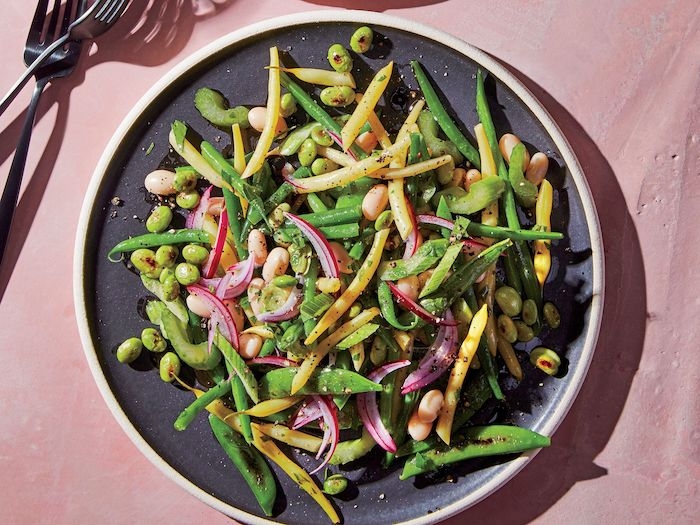 recette salade composee avec des cereales et de l oignon rouge servie dans assiette noire sur nappe rose
