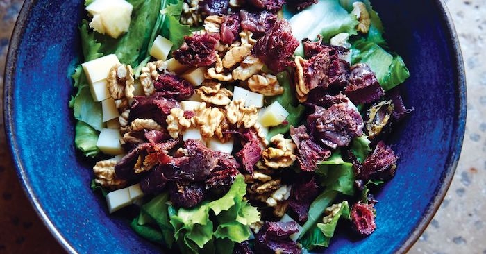 salade a la base des legumes vertes avec des tomates seches et des noix dans une assiette ceramique bleue