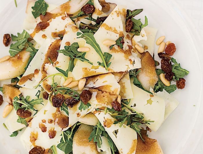 salade de saison de la roquette avec de morecaux de poire et des raisins dans une assiette blanche